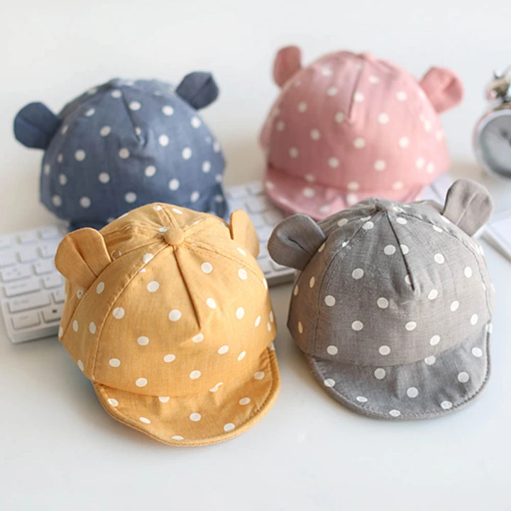 Pastel polka-dot baby hats with little bear ears on cream linen
